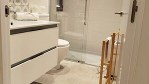 Een moderne badkamer met toilet, douchecabine en een houten droogrek.