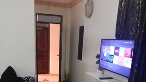 Ett vardagsrum med en tv, ett vitt bord, en liten pall och en mönstrad matta.