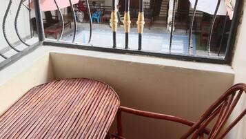A balcony with a table and chairs, a view of the street, and a building with balconies.