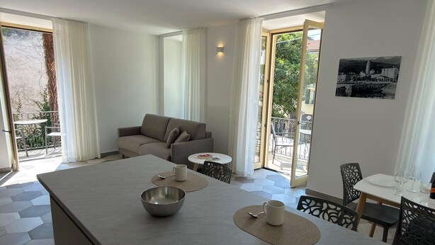 A modern hotel room with a dining area, a sofa, and a balcony with a view. - Baveno Rose Apartment 1 (Baveno)