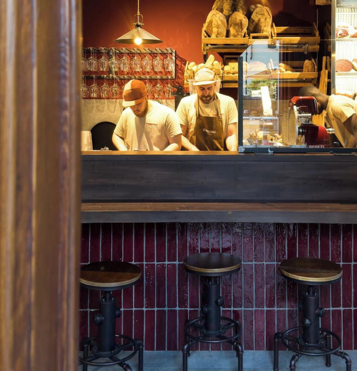 Un espace bar avec des tabourets et un comptoir où deux personnes travaillent.