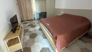 A hotel room with a bed, a desk, a chair, and a television. - Baveno Rose Apartment 1 (Baveno)