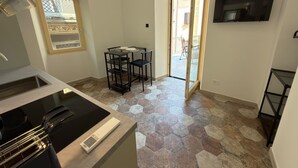 Een kleine keuken met een fornuis, een eettafel met stoelen, een aan de muur bevestigde televisie en een schuifpui naar een buitenruimte.