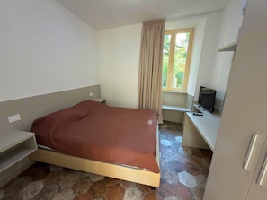 Ein Schlafzimmer mit einem Bett, einem Schreibtisch, einem Fernseher und einem Fenster mit Vorhängen.
