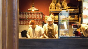 Een bar met krukken en een toonbank, waar twee personen werken.