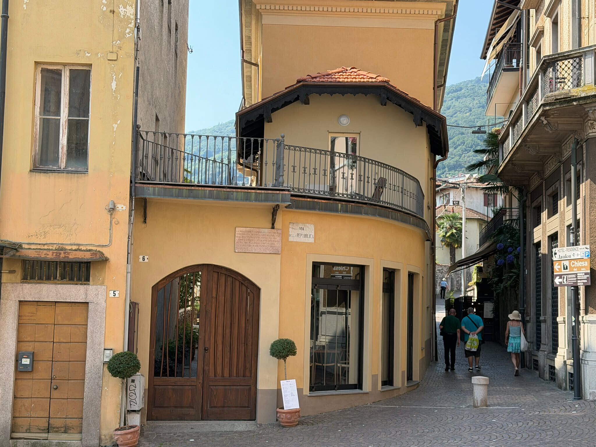 A narrow street with a building featuring a wooden door and a balcony with a metal railing.