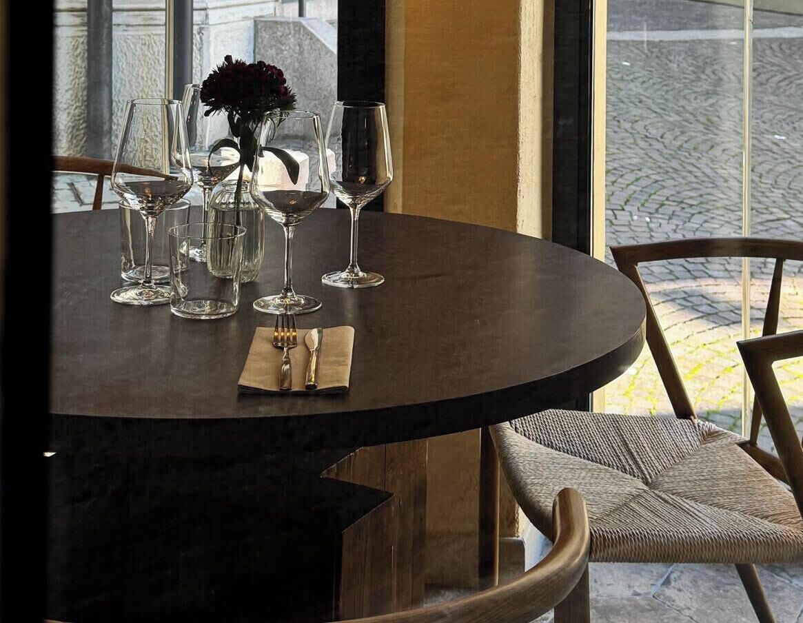 A round table with a vase of flowers, several wine glasses, and a folded napkin.