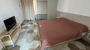 Een hotelkamer met een bed, een televisie op een houten standaard, een kledingkast en een bureau.