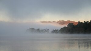 Un lago sereno con una cadena montañosa al fondo, parcialmente oculta por la niebla.