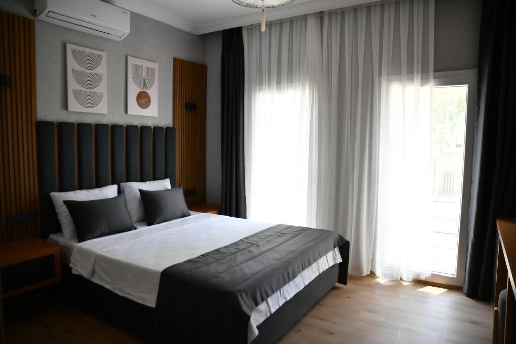 Une chambre moderne avec un grand lit, une tête de lit en bois et une fenêtre avec des rideaux.