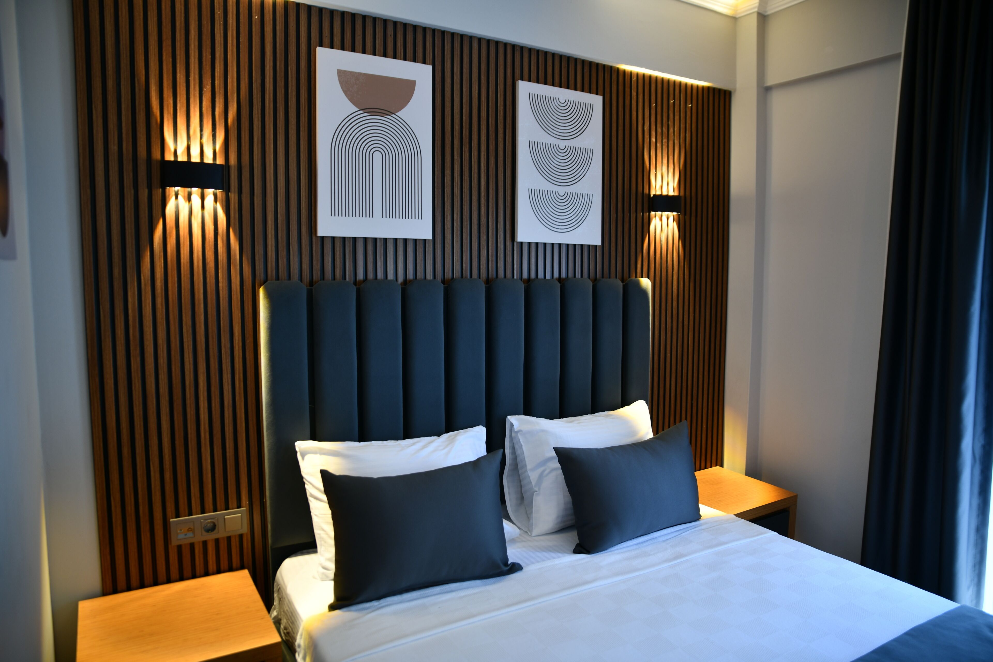A modern hotel room with a large bed, dark headboard, and two bedside tables with lamps.