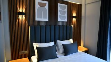 Una habitación de hotel moderna con una cama grande, cabecera oscura y dos mesitas de noche con lámparas.