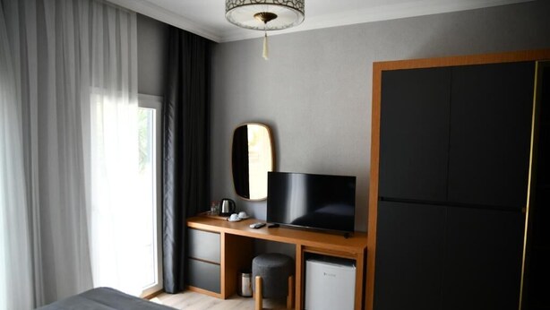 A modern hotel room with a bed, a desk with a TV, a wardrobe, and a window with curtains. - MyElla Marina Hotel (Bodrum)