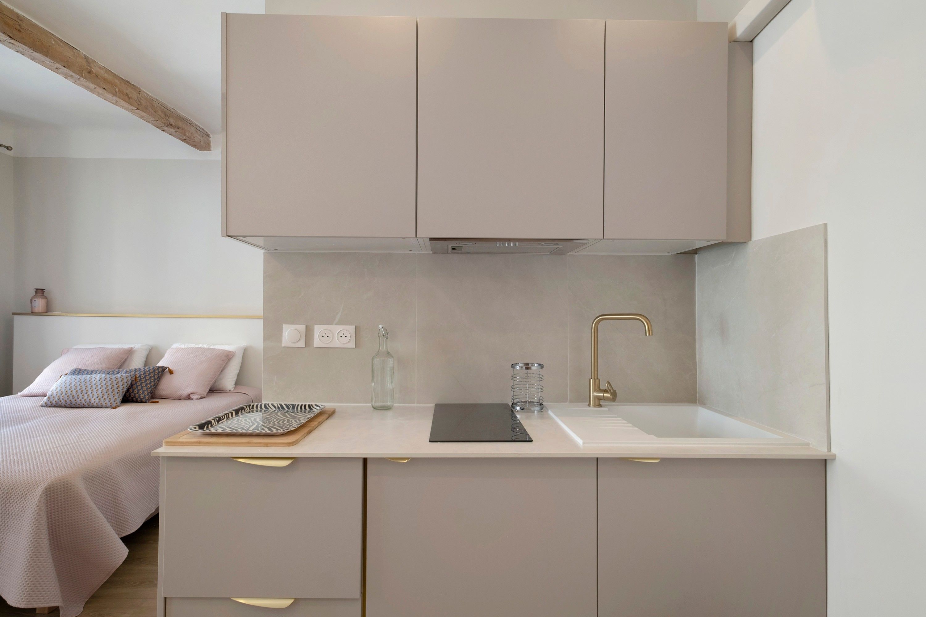 A compact kitchenette with a single sink, a small countertop, and a bed with a headboard in the adjacent room.