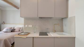 A compact kitchenette with a single sink, a small countertop, and a bed with a headboard in the adjacent room.