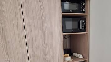 A kitchen with a built-in microwave, a small refrigerator, and a shelf with cups and a bowl.