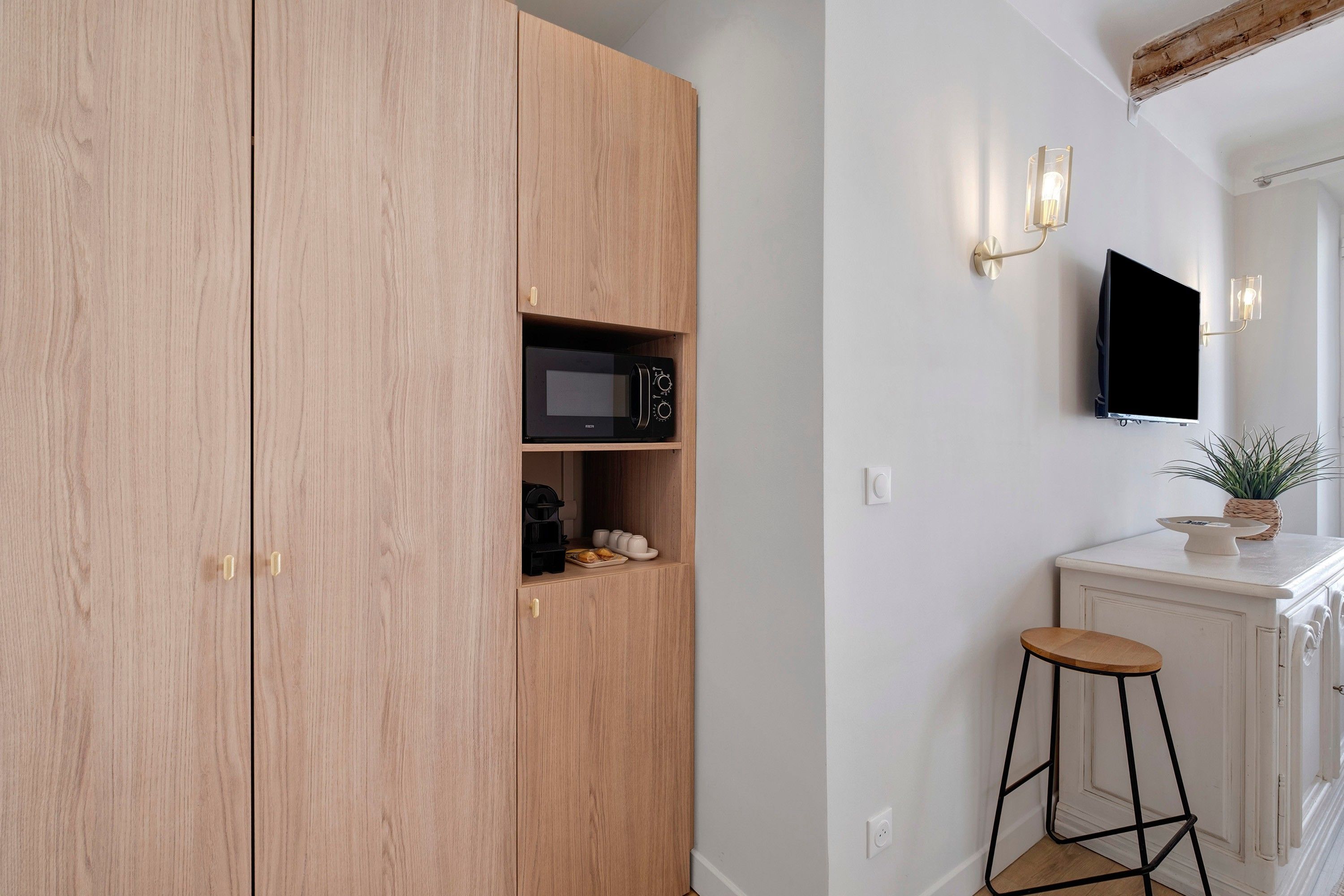 A kitchen with wooden cabinets, a microwave, a coffee maker, and a small bar stool.