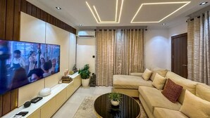 A modern living room with a flat-screen TV, a sofa, a coffee table, and a decorative ceiling light fixture. - 2-Bedroom Luxury Apartment | Fast Wi-Fi | Smart TV | 24/7 Power & Security (Lagos)