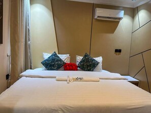 Ett hotellrum med en säng, kuddar, en hoprullad handduk och en luftkonditioneringsanläggning på väggen.