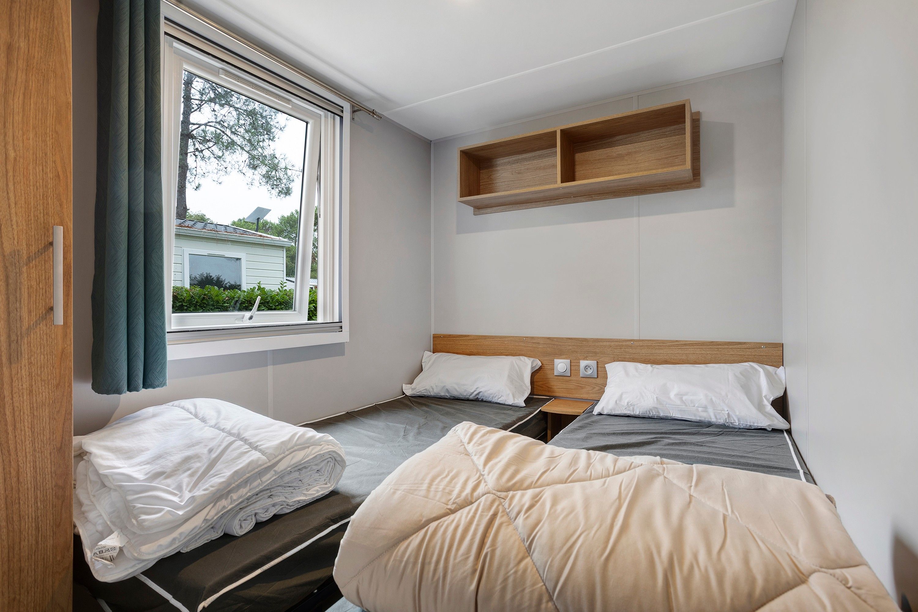 Une chambre individuelle avec deux lits, une fenêtre et une étagère en bois.