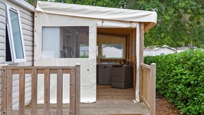 A covered outdoor deck with a wooden railing, a bench, and a wicker sofa. - Mobile Home “On Domaine Kerlann” with Shared Pools and Private Terrace (Pont-Aven)