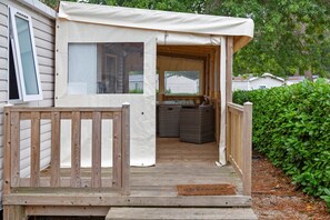 A covered outdoor deck with a wooden railing, a seating area with a sofa and a table, and a view of a house in the background. - Mobile Home “On Domaine Kerlann” with Shared Pools and Private Terrace (Pont-Aven)
