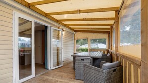 A covered patio with a wooden deck, sliding glass doors, and wicker furniture. - Mobile Home “On Domaine Kerlann” with Shared Pools and Private Terrace (Pont-Aven)