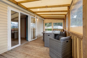 A covered patio area with a sliding glass door leading to a room, a wooden deck, and wicker furniture. - Mobile Home “On Domaine Kerlann” with Shared Pools and Private Terrace (Pont-Aven)