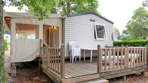 A mobile home with a deck, a covered porch, and a small table and chair. - Mobile Home “On Domaine Kerlann” with Shared Pools and Private Terrace (Pont-Aven)