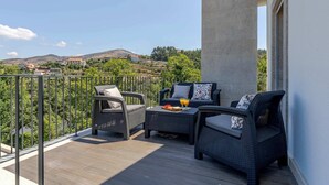 A balcony with wicker furniture, a table with fruit and drinks, and a view of a hilly landscape. - Olival Dream House - Boutique House w/ Pool (Pedorido)