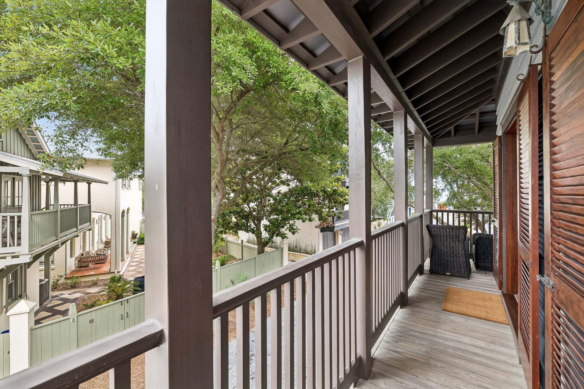 A covered porch with a wooden railing, a bench, and a view of a residential area with trees and a white building.
