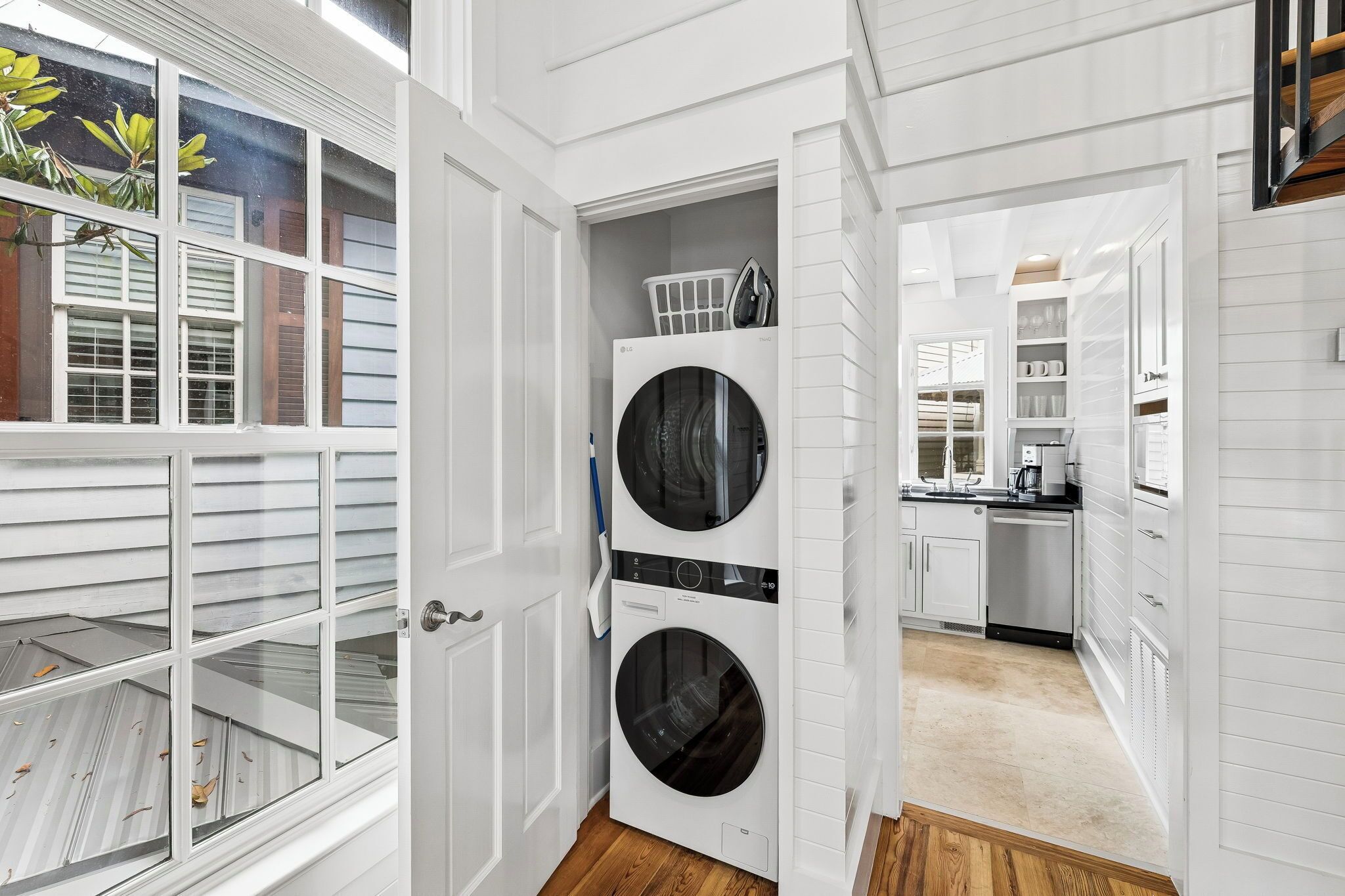 A laundry room with a front-loading washer and dryer, a small laundry basket on top, and a view into the adjacent kitchen area.