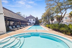 Piscina com espreguiçadeiras e pérgola, cercada por árvores e edifícios.