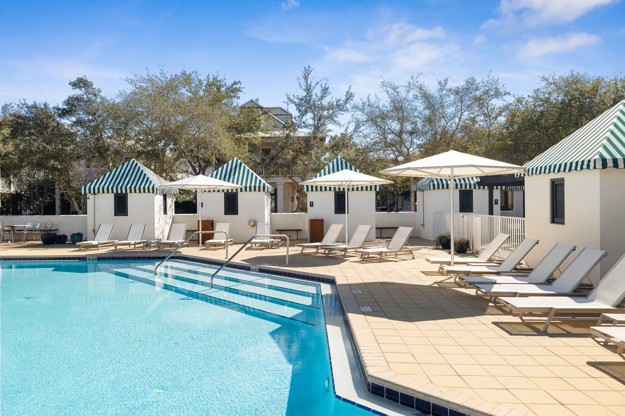A pool area with lounge chairs and small huts with striped roofs.