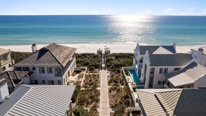 A coastal property with a clear view of the ocean, a pathway leading to a beach, and a swimming pool.