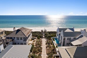 A coastal property with a clear view of the ocean, a pathway leading to a beach, and a swimming pool.