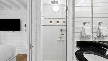A modern bathroom with a glass-enclosed shower, a black sink, and a white toilet.