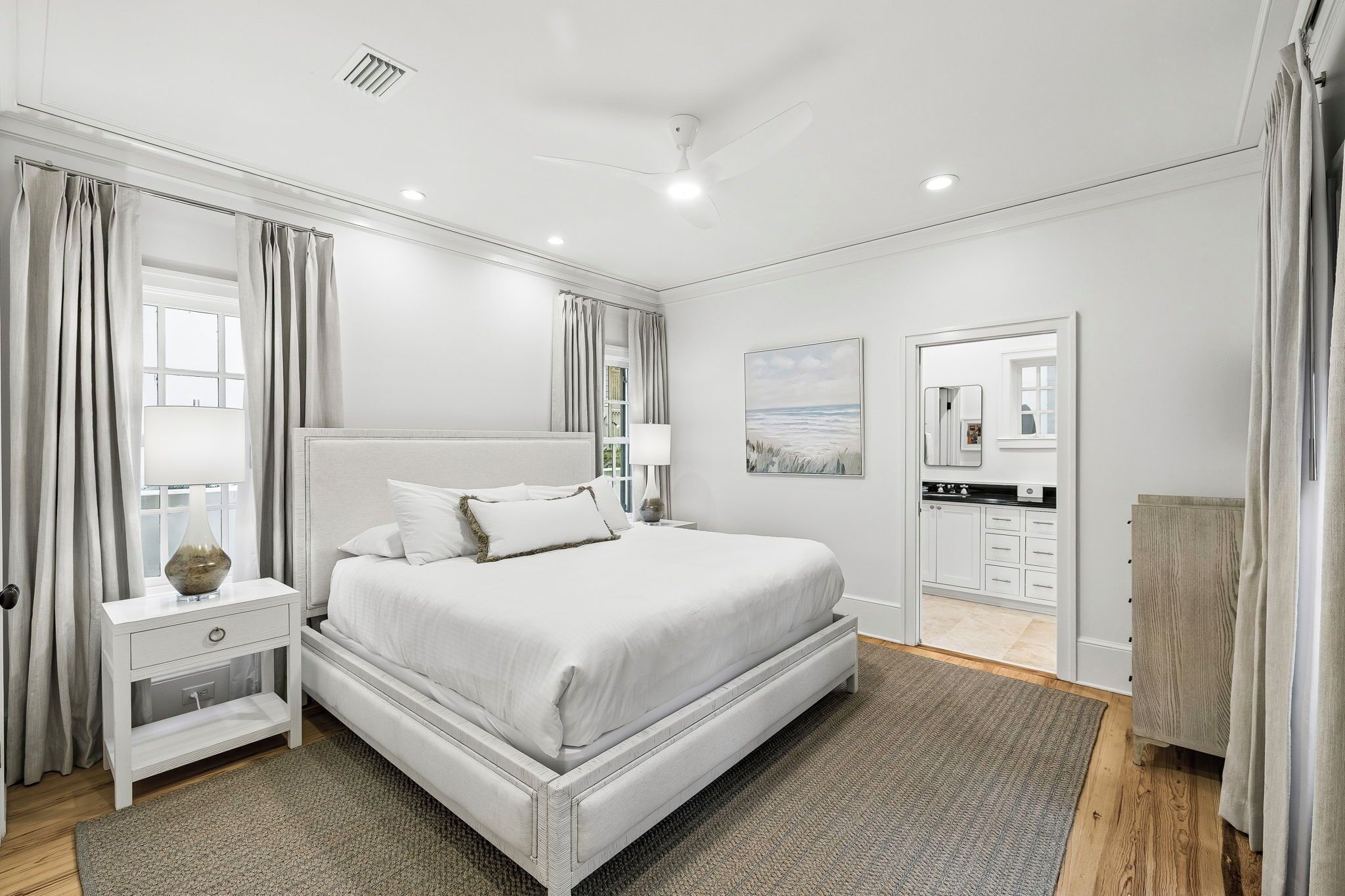 A modern bedroom with a large bed, bedside tables, a nightstand, a mirror, and a view of the bathroom.