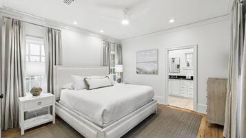 A modern bedroom with a large bed, bedside tables, a nightstand, a mirror, and a view of the bathroom.