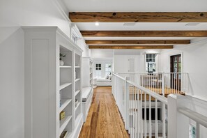 Un couloir aux murs blancs, doté d’un plancher en bois et d’un escalier avec des rampes blanches.