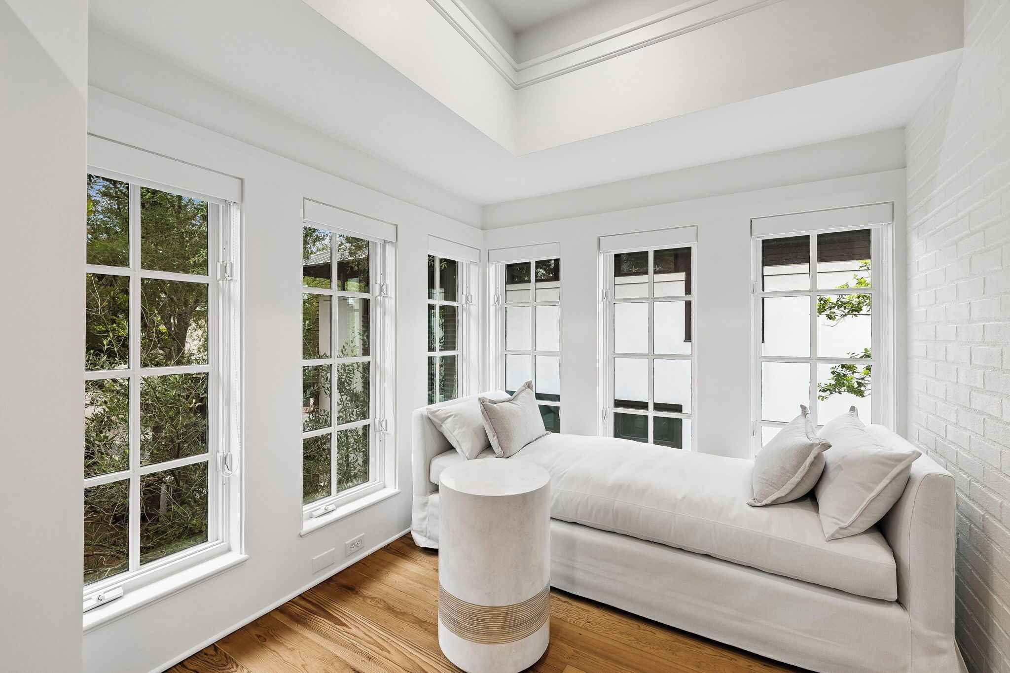 A room with a white sofa, a round side table, and large windows with white frames.