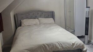 Et soveværelse med seng, garderobeskab, varmeblæser og en lampe i loftet.