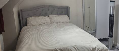 Un dormitorio con cama, armario, calefactor y lámpara en el techo.
