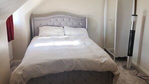 Et soveværelse med seng, garderobe, varmeblæser og skråt loft.