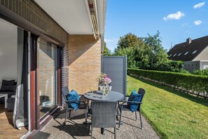 Eine Terrasse mit Tisch und Stühlen, eine Glastür und eine Ziegelwand.