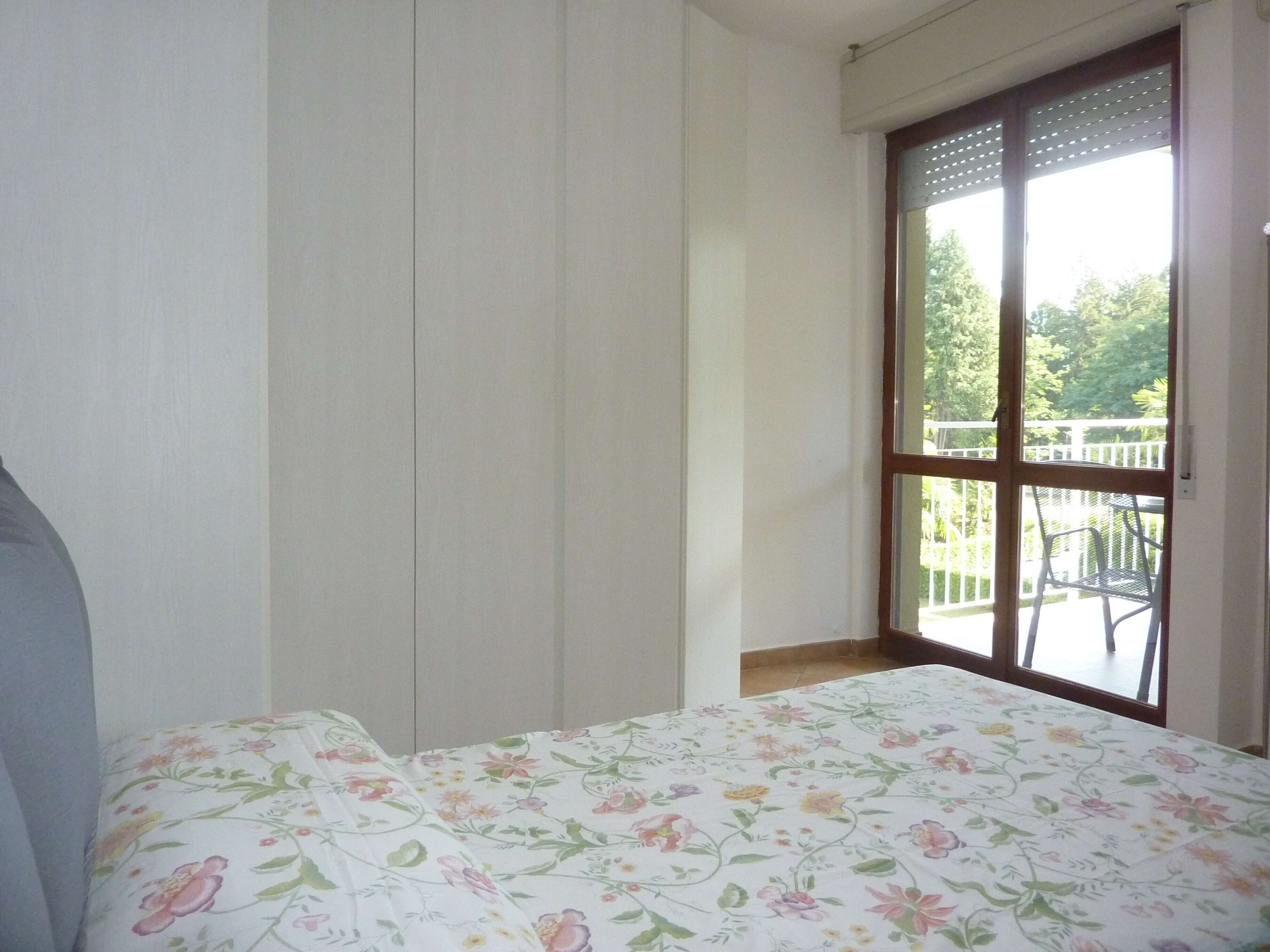 Une chambre à coucher avec un lit, une fenêtre donnant sur un balcon et une porte.