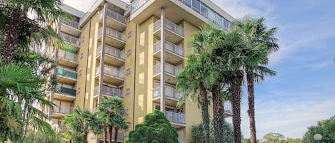 A multi-story residential building with balconies, surrounded by palm trees and a well-maintained lawn.