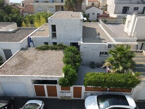 A residential building with a flat roof, a garage with wooden doors, and a small garden area with a palm tree. - Large family home with spacious, landscaped terraces, 100 meters from the beach (Mauguio)