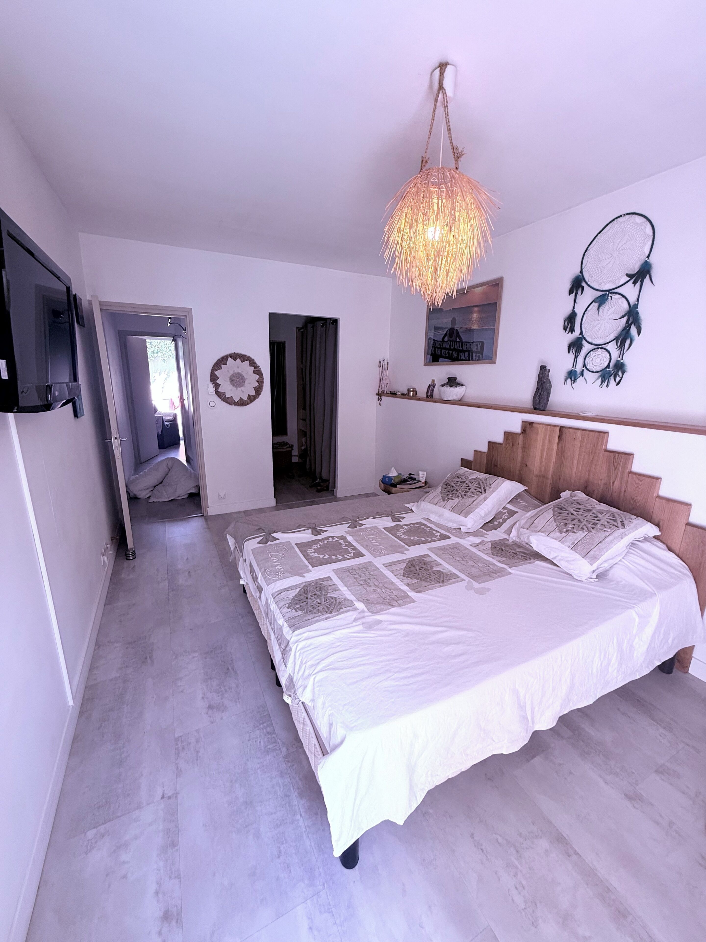 Une chambre avec un grand lit, un téléviseur fixé au mur et un luminaire au plafond.