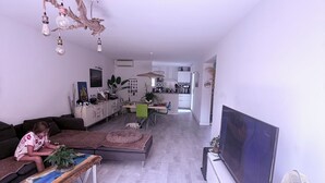A modern living room with a flat-screen TV, a dining area with chairs, and a kitchen in the background. - Large family home with spacious, landscaped terraces, 100 meters from the beach (Mauguio)